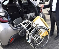 「車いす収納装置」の操作風景。車内に収納するには、折り畳んだ車いすのフロントを写真のように持ち上げてフックに掛け、電動スイッチを入れるだけ。