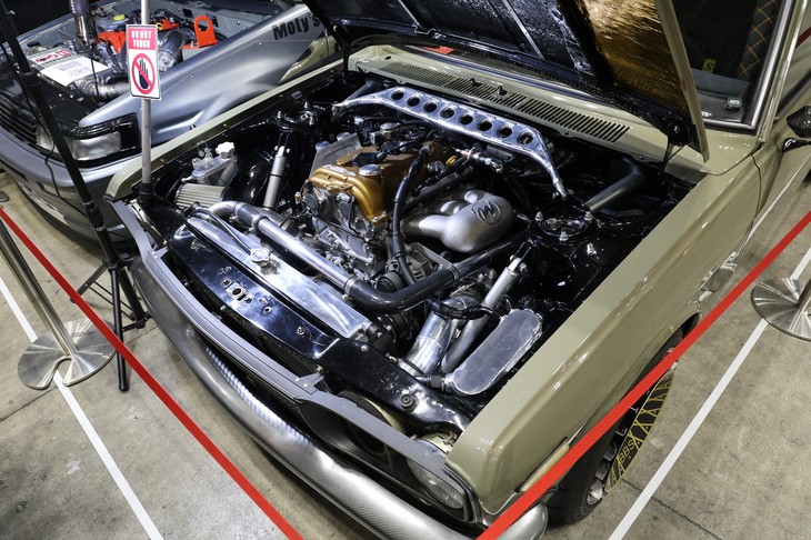 型式名510こと3代目「ダットサン・ブルーバード」のエンジンを現行「GRヤリス」用1.6リッター直3 DOHC 12バルブターボのG16E-GTSにスワップ。ボンネットが低い旧車に現代のロングストローク型ユニットを収めるため、ボンネットの一部をバルジ化している。隣の「AE86」も同じくG16E-GTSを積んでいる。