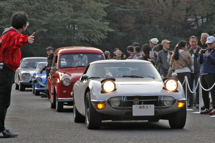 全プログラムが終了、日が傾きかけた中、ギャラリーに見送られて順不同で会場を後にする一般参加車両。「練馬5」のシングルナンバーを付けた1969年「トヨタ2000GT」に1956年「オースチンA35カントリーマン」などが続く。