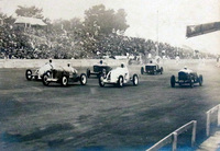 84年をさかのぼる1937年5月に開かれた第3回全日本自動車競争大会における商工大臣杯(国産小型車によるレース)のスタートシーン。満員の観衆が座っているのは、今も残るコンクリートの観客席である。