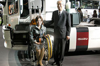 いすゞ自動車の井田義則社長(右)の後ろには、トラックの福祉車両「ギガマックストラクタAC(アクティブキャブ)」。リモコンでドアを開け、リフトに車椅子を固定、上がりきったら90度回転し乗車完了となる。