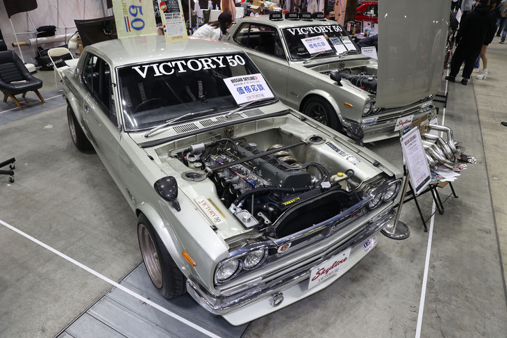 ハコスカ一筋30年以上、L6もS20も知り尽くしたVICTORY 50がつくった“究極の「GT-R」仕様”という「日産スカイライン ハードトップ2000GT」(KGC10、手前)。フルレストアされたボディーに積まれた直6 DOHC 24バルブのOS技研製TC24-B1Zの3.2リッターウェバーφ50仕様はベンチ実測で最高出力400PS/8000rpmを発生するそうで、価格は3000万円。奥のSOHCのL6仕様は1500万円だそうだから、ほぼエンジン代で2倍になるわけだ。ちなみに新車価格もL20搭載のGT(KGC10)の89.5万円に対してS20搭載のGT-R(KPGC10)は2倍近い154万円だった。なお2台の間にあるタコ足は、OS技研、トラスト、VICTORY 50の3社共同開発によるL6用とのこと。