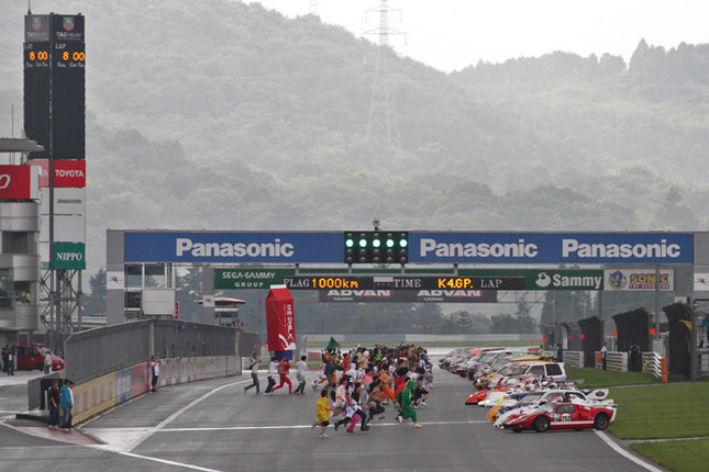 夜半から降ったりやんだりの雨が、小康状態だった午前8時にレースはスタート。スタート方式は仮装したチームメンバーがマシンに駆け寄り、安全確認シールをはがしてから発進するという変則ルマン式。1リットルの牛乳パックに扮(ふん)したメンバーは、さすがに重くてひとりでは走れず、ヘルパー付き(笑)。