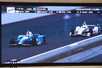 会場で放映された、今回のインディ500を振り返る映像から。レース終盤、首位に立った佐藤(写真左)が、優勝に向かってラストスパートをかける。