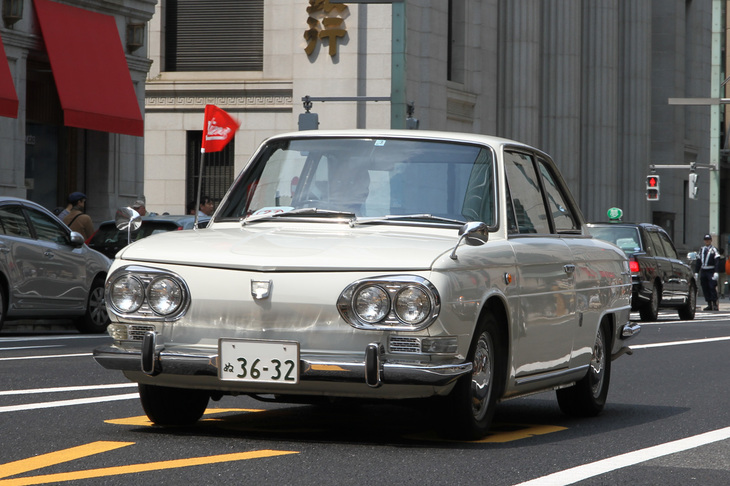 オーナーズクラブで製作したという「Hino」のロゴ入りフラッグをなびかせて走る1966年「日野コンテッサ1300クーペ」。「ルノー4CV」のライセンス生産から始まった日野自動車の最後の乗用車。ミケロッティの手になるボディーのリアに直4 OHVクロスフローの1.3リッターエンジンを搭載。