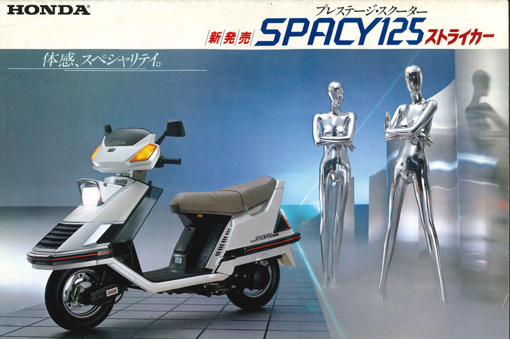 「ゴールドウイング」に限らず、コンフォート系バイクというものはどれも「クルマになりたい」ムードが感じられるものだ。写真の「ホンダ・スペイシー125ストライカー」（1983年）もその典型で、カタログ（写真）には“四輪的うたい文句”があふれる。
	 