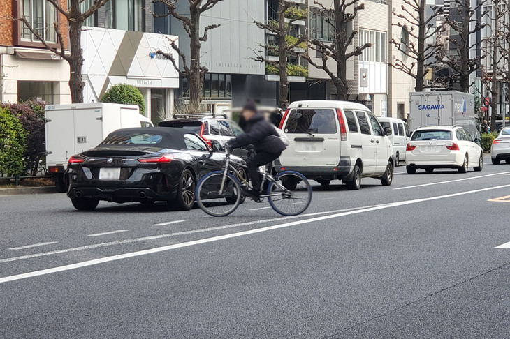 2026年1月中旬、東京・渋谷区の某所にて、ビュンビュンとクルマが行き交う大通りを平然と斜め横断する自転車。「いざとなったらクルマの側が止まってくれる」と考えているのかもしれないが……。