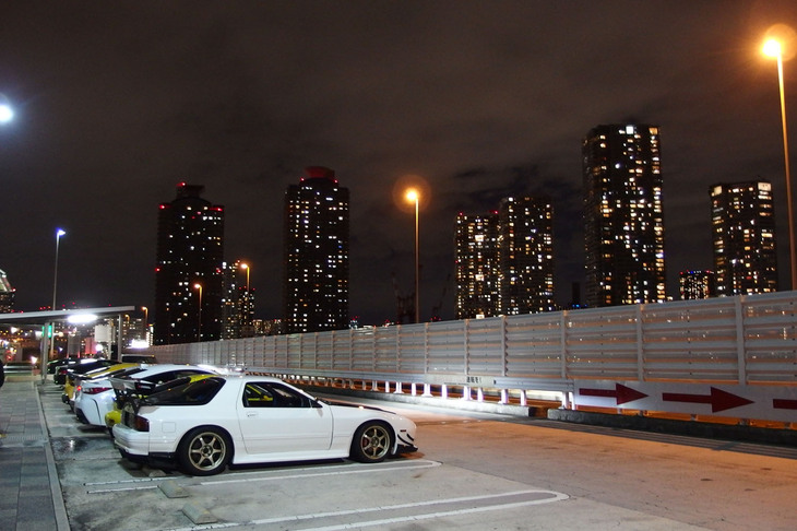 大きなリアウイングや大径ホイールなどでカスタマイズされた「RX-7」や「スープラ」が並んだ辰巳PA。これらのチューンドカーは、アジア系とおぼしき若い外国人がドライブしていた。