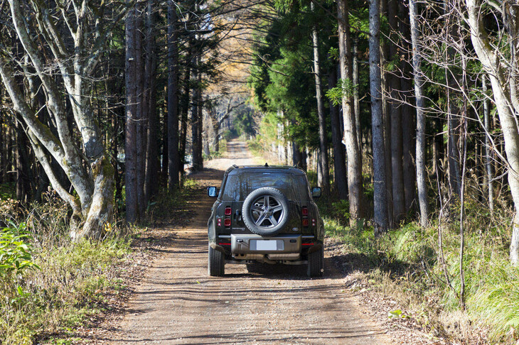 針葉樹が立ち並ぶ林道を行く「ディフェンダー110」。走行の様子はオフィシャルカメラマンによって撮影されており、イベント終了後に画像データが参加者にプレゼントされる。