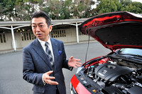 実車を前に開発エピソードを語る梶山さん。本文中の「奇妙な形状のパーツ」とは、事故などの際に衝撃を緩和するため、エンジンルームの左右の縁に備えられたクッション部品のことだ。