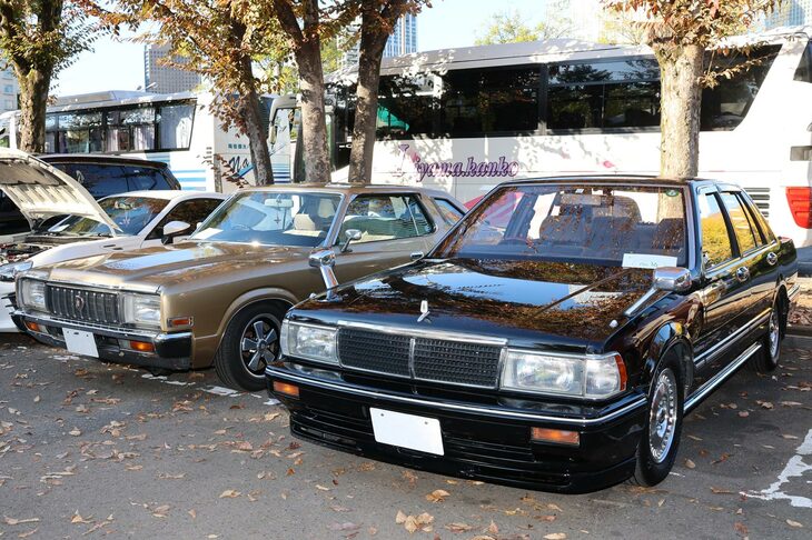 世代を超えて国産サルーンのライバルが並ぶ。5代目「トヨタ・クラウン」（写真向かって左）が2ドアハードトップということにも驚きだが、7代目「日産セドリック」（同右）のセダンが、レアな“ベンコラ（ベンチシート＋コラムシフト）仕様”なうえ、オーナーが若い女性だったことにも驚かされた。