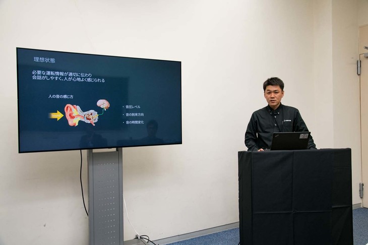 「マツダ3」の静粛性向上技術について説明したNVH開発部の大槻修平氏。マツダ3では振動エネルギーを集めて減衰するという考え方を採り入れており、車両の各部に「減衰節」というパーツを装着している。