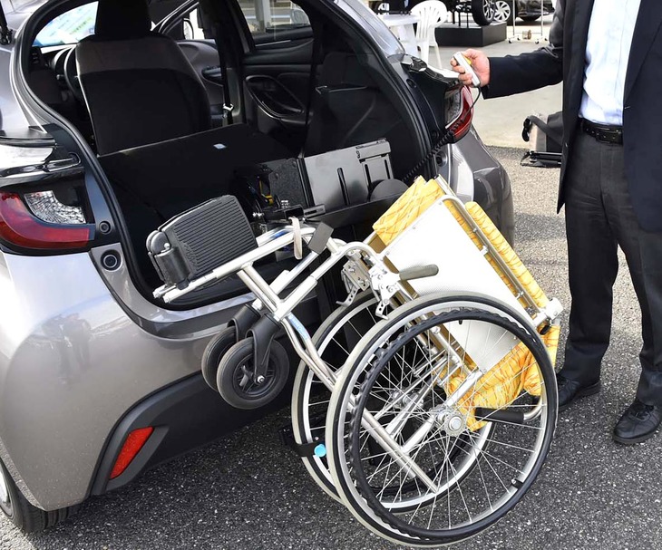 「車いす収納装置」の操作風景。車内に収納するには、折り畳んだ車いすのフロントを写真のように持ち上げてフックに掛け、電動スイッチを入れるだけ。