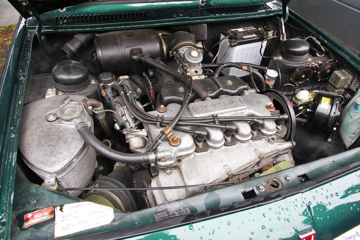 「ホンダ1300 77デラックス」のエンジンルーム。DDACエンジンのシリンダーヘッドとブロックは、アルミで一体鋳造されたエアジャケットと呼ばれる外壁に覆われており、エンジンとエアジャケットの間を、ファンによって送られた空気が通過して強制冷却される。走行中は導入された外気によってもエンジン外壁は冷却されるため、強制空冷と自然空冷を合わせて二重空冷というわけだ。77はシングルキャブレター仕様で、1298cc直4 SOHCから最高出力100ps/7200rpm、最大トルク10.95kgm/4500rpm（いずれもグロス値）を発生。ちなみにそれまで1.3リッター級の量産市販車で最も高出力だったアルファ・ロメオの「1300」系や「ランチア・フルヴィア」のスポーツモデルでも90ps前後だったから、少なくとも額面上のパワーにかけては、H1300は世界最高峰だったのだ。