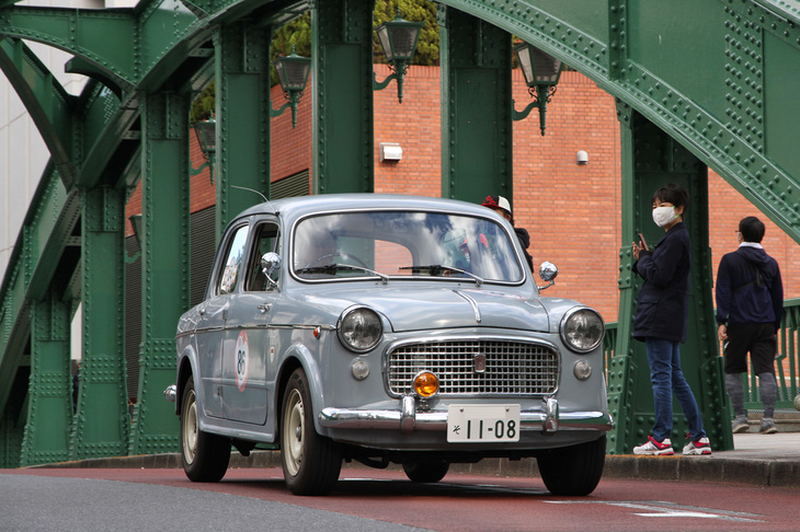 柳橋を渡る1962年「フィアット1100ベルリーナ」。フロントドアが前開きで、前後ドアはセンターピラーを支柱に観音開きと逆に開く。