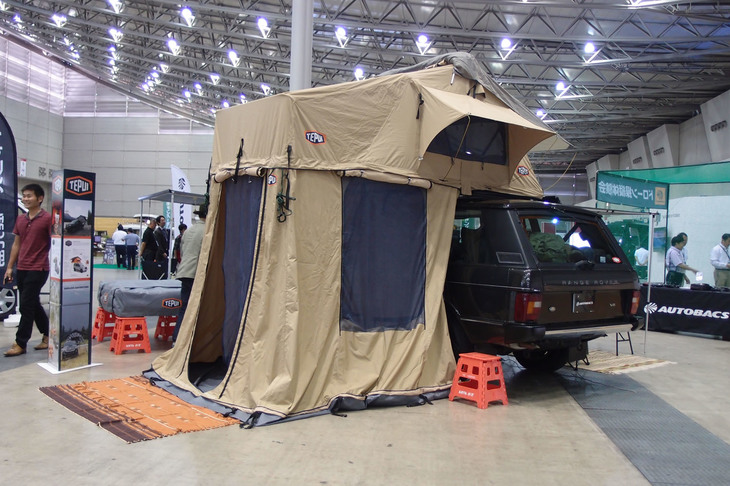 「レンジローバー」をすっぽりと覆っているのは、「TEPUI（テプイ）」と呼ばれるルーフトップ型テント。写真奥に見えるグレーのパッケージが収納時のもので、これをクルマのルーフに載せた状態から展開すると、ご覧のとおりベージュの大きなテント（3人用）が組みあがる。