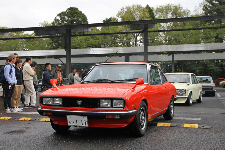 閉会式終了後、参加車両はギャラリーに見送られながら雨上がりの会場を後にする。これは1979年「いすゞ117クーペ」。俗に量産角目と呼ばれる後期型である。