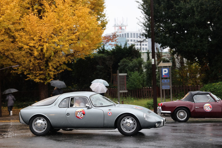 いちょう並木から神宮外苑の周回路に入る、世界初の市販ミドシップスポーツである1964年「ルネ・ボネ・ジェット」。前方は1965年「トライアンフ・スピットファイア」。