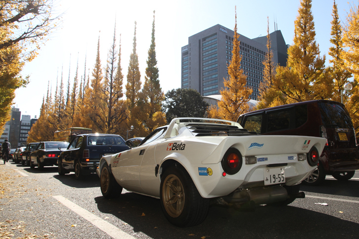 パレードコースは、いちょう並木が突き当たる青山通り（国道246号）を左折。土曜なので絶対的な交通量は多くないのだが、いちょう見物にやってくる人々の横断待ちでなかなか左折できないため、ご覧のように渋滞する。後端は1975年「ランチア・ストラトスHF」。