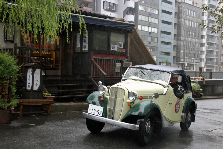 1952年「ダットサン・スポーツDC-3」。戦前型から続くトラックと共通シャシーの「ダットサン」をベースに、日本で初めてスポーツを名乗ったモデル。向こう岸に並ぶビル群がなければ、タイプスリップしてしまったような光景だ。