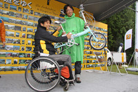 「エッフェル塔は東京タワーより高い。ウィかノンか？」という問題から始まった「ルノージャポン・ウルトラクイズ」の優勝者に、ゲストの青木琢磨氏から賞品のルノー・ブランドの折り畳み自転車が渡された。後ろのパネルに貼られた写真は、「カングー日本の道を行く」と題された来場者によるフォトコンテストの応募作品。