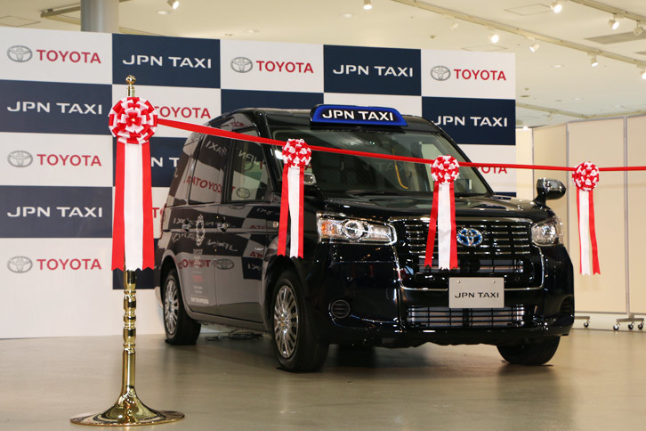 会場にて、ステージの脇でテープカットを待つトヨタの新型タクシー「JPN TAXI（ジャパンタクシー）」。