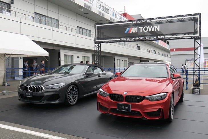 会場エントランスに設けられた「WELCOM TO M TOWN」のサインと、その下に展示されていた「M8」（左）と「M4」（右）。「Mタウン」とは、ハイパフォーマンスカーのための仮想都市という設定で、BMWの世界観のひとつをユニークに表現している。現在同社のウェブサイトでMタウンに関する動画が数本公開されている。今回のイベントはそのMタウンの仮想世界と現実をつなぐというコンセプトも持ち合わせているという。