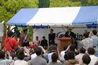 オープニングセレモニーでオーナーやファンを前に挨拶するMr. K。隣は右から順に伊藤町長、かつての“（初代）Z遣い”柳田春人さん、その御子息で自身も現代のZを操り“スーパーGT”を闘う柳田真孝選手。