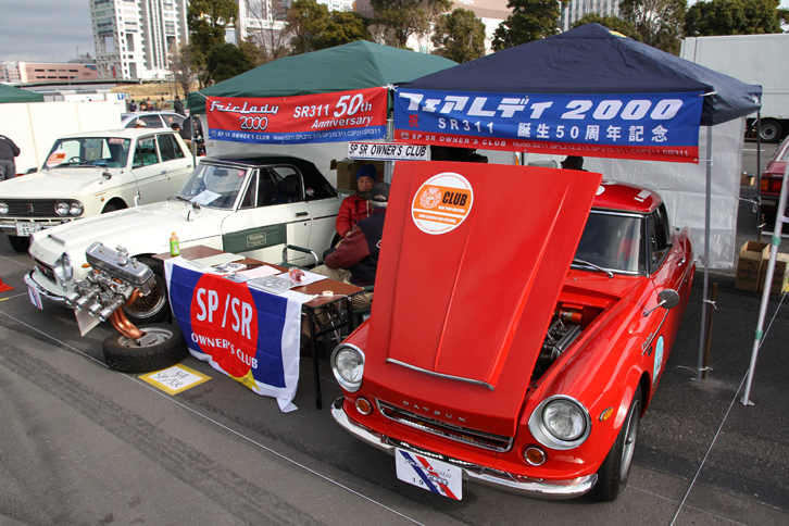 「ダットサン・フェアレディ1500」（SP310）、「同1600」（SP311）、「同2000」（SR311）および「日産シルビア」（CSP311）のオーナーが集う、SP/SRオーナーズクラブ。今回はSR311の誕生50周年を記念して、紅白の2台（前期、後期）を展示。日本車で唯一、φ44のソレックス・ツインチョークキャブレターを2連装した2リッター直4 SOHCのU20型エンジンのヘッドも飾っていた。