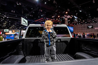 巨大なピックアップトラックの荷台に乗り、カメラに向けて笑顔を見せる男の子。