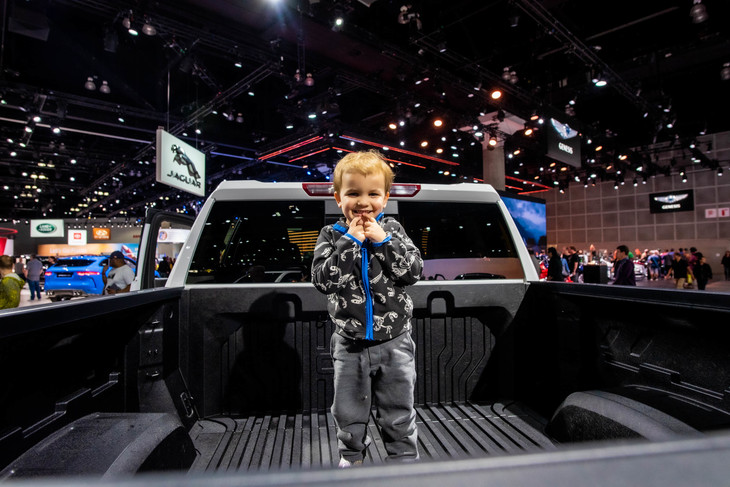 巨大なピックアップトラックの荷台に乗り、カメラに向けて笑顔を見せる男の子。