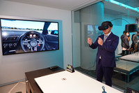 VRゴーグルと大型スクリーンには同じ映像が表示される。体感中は写真の人のようにステアリングホイールを握れそうな感覚を覚えるが、手を伸ばしても触感はない。