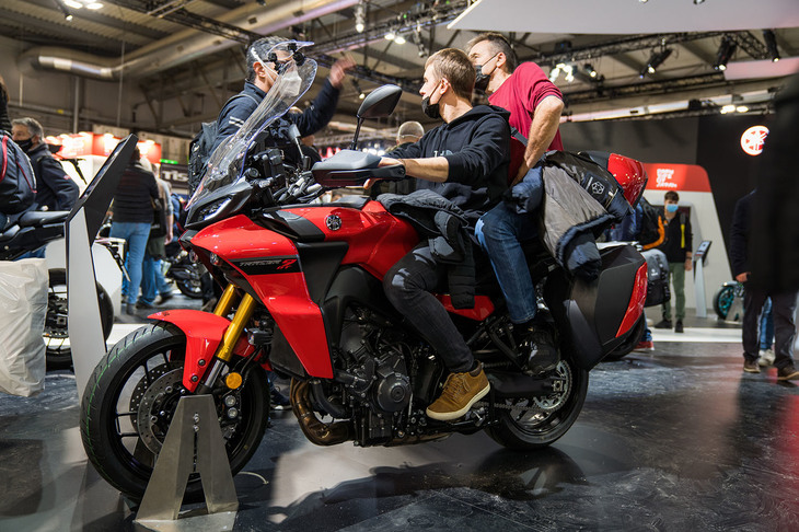 典型的な「EICMA」の景色。まわりに“またがり待ち”の人がいなければ、このままの状態で10〜15分ほど仲間と話し込むことも。身ぶり手ぶりを交えて盛り上がった議論の前半は「ヤマハ・トレーサー9 GT」についてだが、タンデムシートの男性がスマホをいじり始めた後半は、まったく違う話題で盛り上がっていたと想像する。