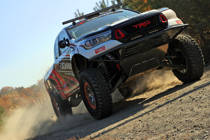 林道を豪快に走るオフロードレース仕様の「ハイラックス」。レギュレーションの違いもあり、サスペンションには2021年に持参した「トヨタ・ハイラックス タッツフィンクデザートレースEX4クラス優勝車両」のおよそ2倍（！）ものトラベル量があるという。