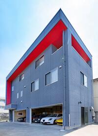 外壁のグルーグレーに軒裏のレッドが生える。まるでモダンアートのような色使いは、建物のデザインがシンプルなだけに一層際立つ。