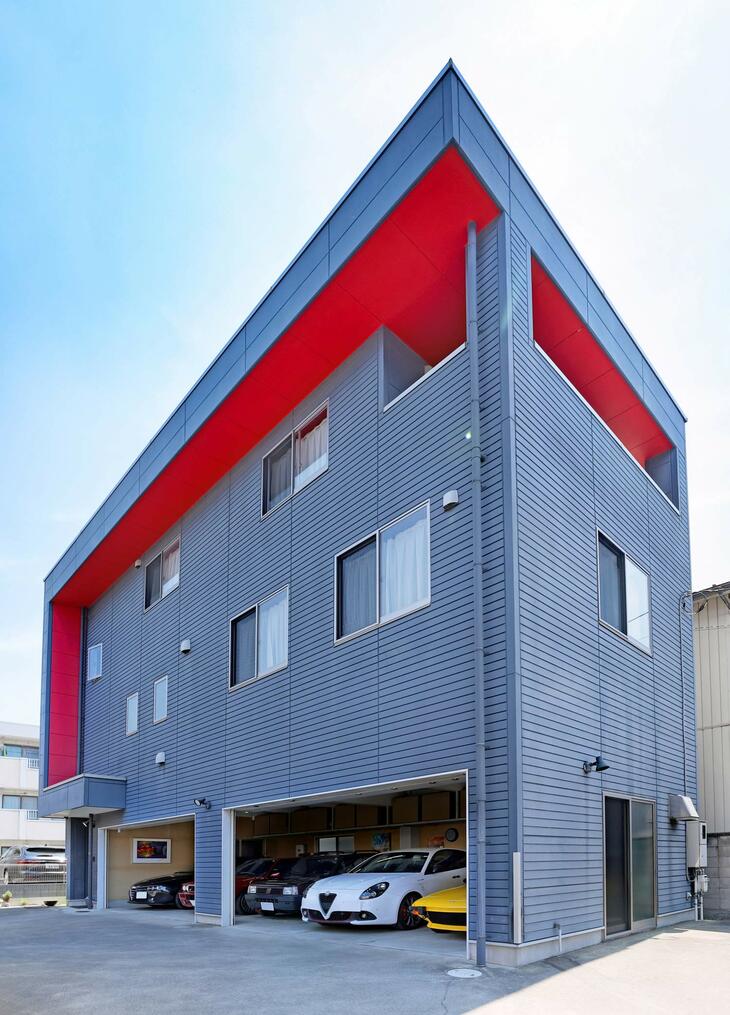 外壁のグルーグレーに軒裏のレッドが生える。まるでモダンアートのような色使いは、建物のデザインがシンプルなだけに一層際立つ。