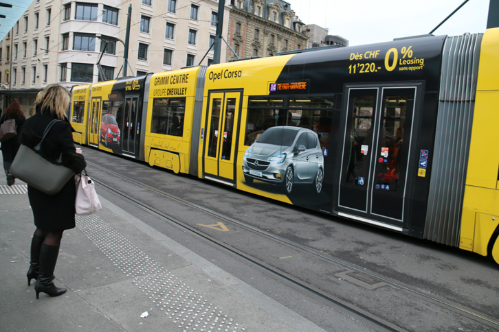 ジュネーブの市電は、地元の自動車ディーラーによるラッピング広告が盛んだった。これはオペルのもの。それによると「コルサ」の価格は1万1200フラン（約125万円）からで、「リースは前払い金なし」の脇には極めて小さな「*」印が見られる。詳細は電車のどこに書かれているのか……？