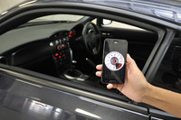 「写真奥に見える『86』のエンジン回転数を、スマートフォン上に表示する」デモの様子。ゆくゆくは水温などのデータまで採取・蓄積できるようにし、「ドライビング・アプリ」として活用することも検討されている。