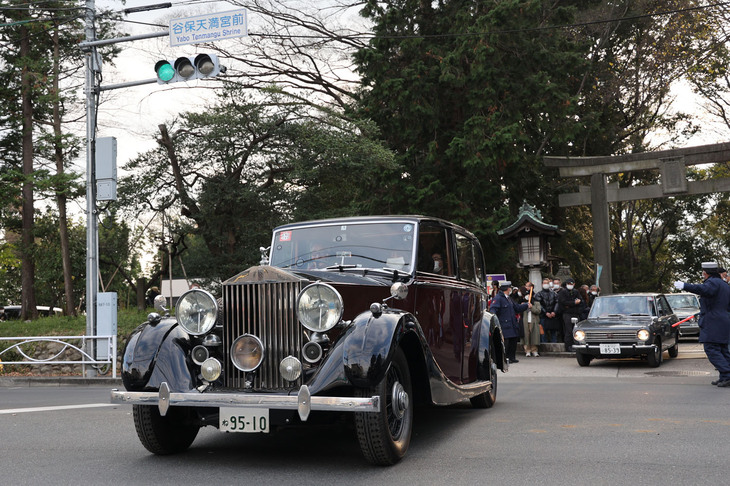 谷保天満宮を出ていく1939年「ロールス・ロイス・シルバーレイス」。ボディーは御料車にも使われていたマルーンに近い溜色（ためいろ）と黒のツートーンで塗られている。続くのは1967年「ダットサン・サニー1000」。