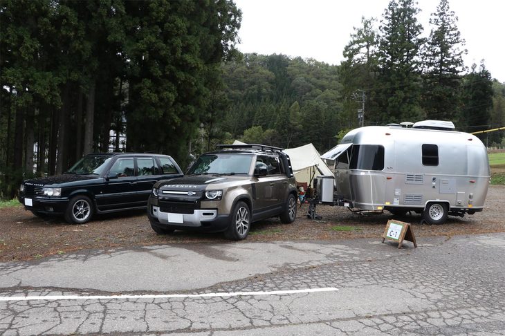 会場内にはキャンプサイトが設けられ、キャンピングトレーラーや大型テントを設置して、宿泊を楽しむオーナーの姿も見られた。こちらは米エアストリームのキャンピングトレーラーをけん引する現行型「ディフェンダー110」（手前）と、第2世代の「レンジローバー」（奥）。往年の英国車の趣を残す2代目レンジローバーは、今は“クラシックレンジ”こと初代の陰に隠れている感もあるが、やはり端正で均整のとれたデザインが美しく魅力的だ。