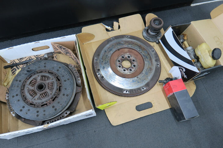 今回交換した主要部品一式。左からクラッチプレート、フライホイール、クラッチレリーズシリンダー、ブレーキマスターシリンダー。右下の箱に入っているのと、クラッチプレートの上にひっそりと置かれているのが、分解された左リアのインナーロッド。