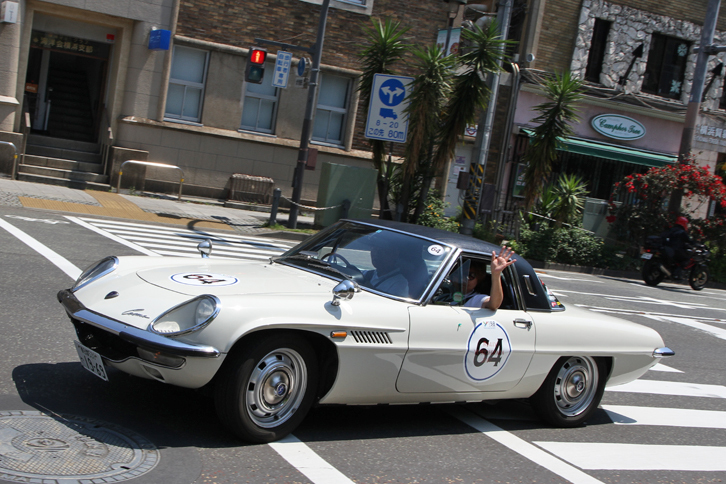 神奈川県庁舎などが立ち並ぶ、日本初の西洋式街路である日本大通りに向かって左折しようという1969年「マツダ・コスモスポーツ」。