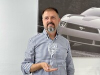 イタルデザイン社ビジネス開発担当のコッラード・ベッキオ氏。アルタランガ・ワイン協同組合のために同社がデザインしたグラス（2022年）とともに。2024年7月、筆者撮影。