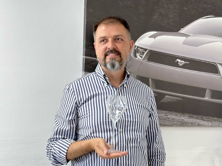 イタルデザイン社ビジネス開発担当のコッラード・ベッキオ氏。アルタランガ・ワイン協同組合のために同社がデザインしたグラス（2022年）とともに。2024年7月、筆者撮影。