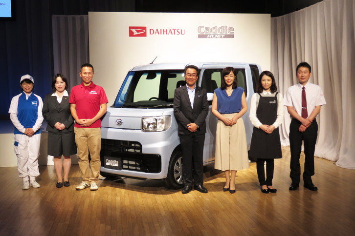 ダイハツ工業の上田 亨上級執行役員（写真中央、スーツの人物）と、タレントの菊池桃子さん（同右から3番目）、およびヒアリングや試験運用などを通して、「ハイゼット キャディー」の開発に協力した5社（アートコーポレーション、ダスキン、ドコモ・バイクシェア、花キューピット、プレナス）の担当者。