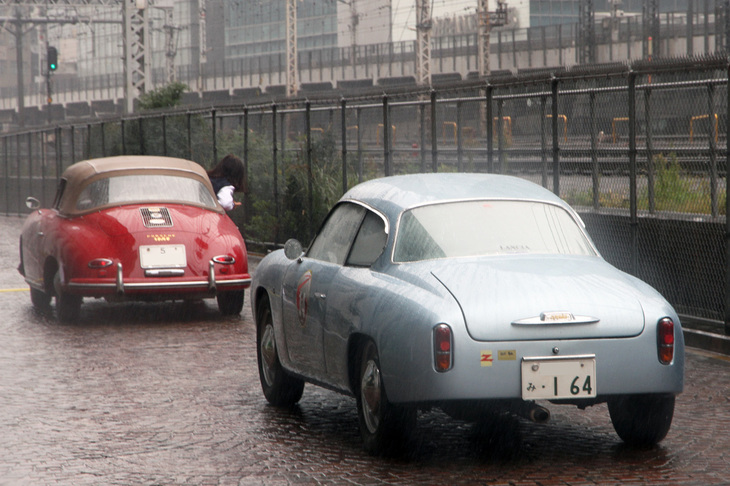 スタートから間もない地点で、最初の“線踏み”（タイヤで計測センサーが仕込まれた線を踏むことから、俗にPC競技のことをそう呼ぶ）が行われる。ドライバーに線踏みのタイミングを指示すべく、コドライバーが身を乗り出している1958年「ポルシェ356Aカブリオレ」は、単に「5」から始まる時代の東京ナンバーを付けた、現存する唯一のポルシェ。順番を待っているのは1960年「ランチア・アッピアGTEザガート」。