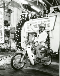 「スーパーカブ」にまたがる本田宗一郎（1906-1991）。写真は1971年に鈴鹿製作所で行われた、二輪累計生産1000万台達成セレモニーでのもの。