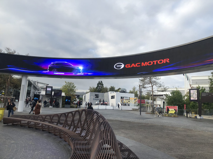 モーターショー会場であるポルト・ド・ヴェルサイユ見本市会場入り口付近の広場。巨大サークル状の電光掲示板には広告が投影される。スペインのセアトはともかく、もうひとつはなんとパリショー初参加であるGAC（広州汽車集団）のものであった。