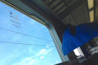 「エアコン付き車両です。非常時以外開けないでください」と記してあるものの、暑さに耐えかねた誰かによって窓は開けられ、風でカーテンが踊る。