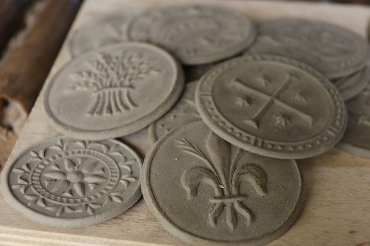 作業の途中で、粘土に押してみては彫り具合をチェックする。右手前のユリの図柄はフィレンツェのフィオリーノ通貨をモチーフにしたもの。